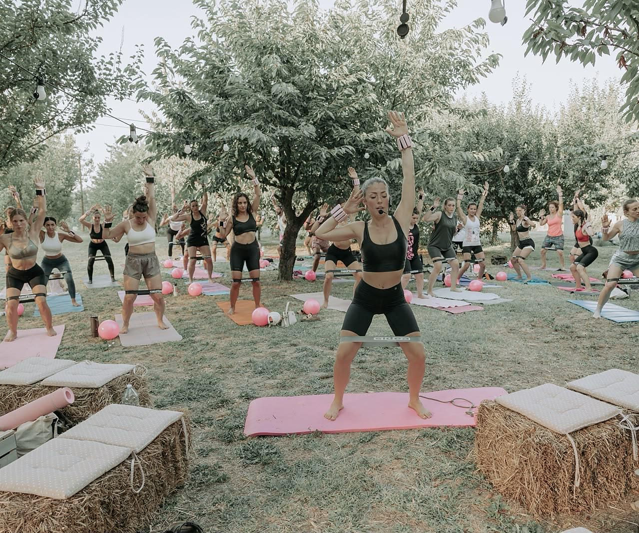 Laurona guida una lezione di pilates all'aperto nel frutteto, tra balle di fieno
